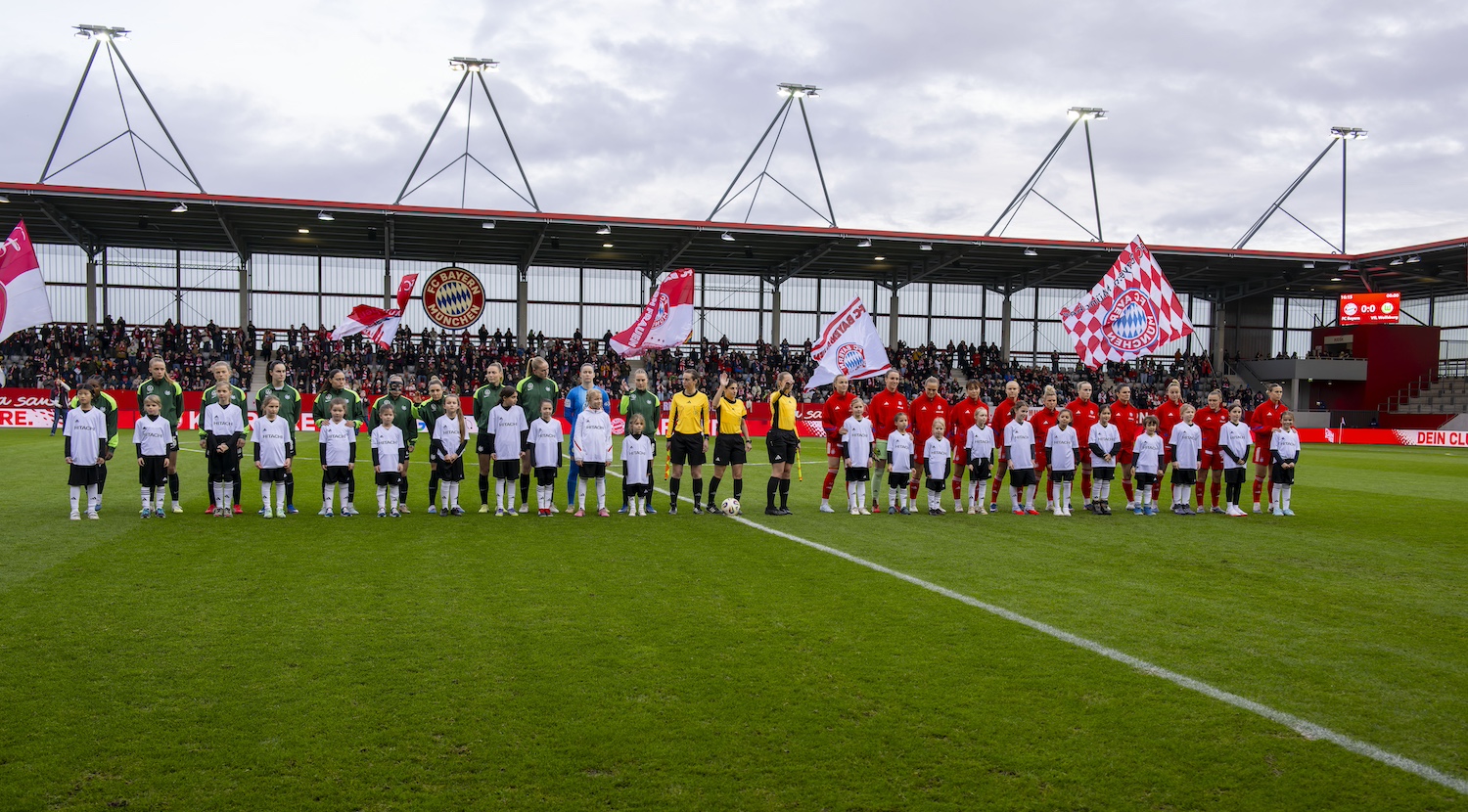 Die Frauen-Fußballmannschaften des FC Bayern und VfL Wolfsburg mit Einlaufkindern von "Mädchen an den Ball" auf dem Spielfeld