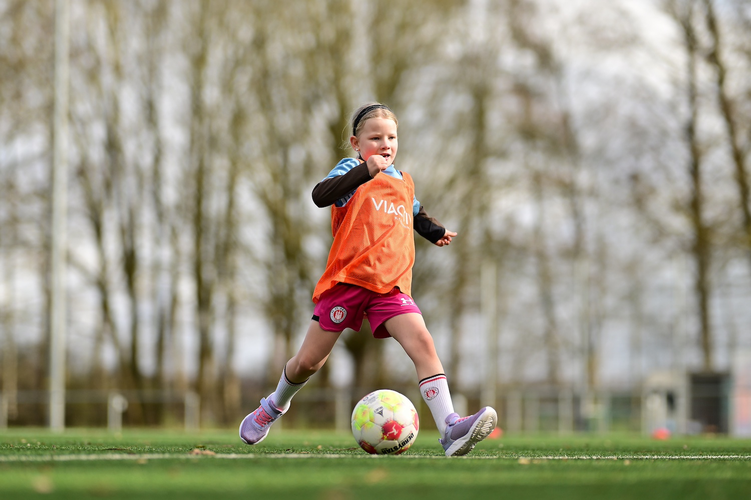 Ein Mädchen in orangefarbenem Leibchen tritt gegen einen Fußball
