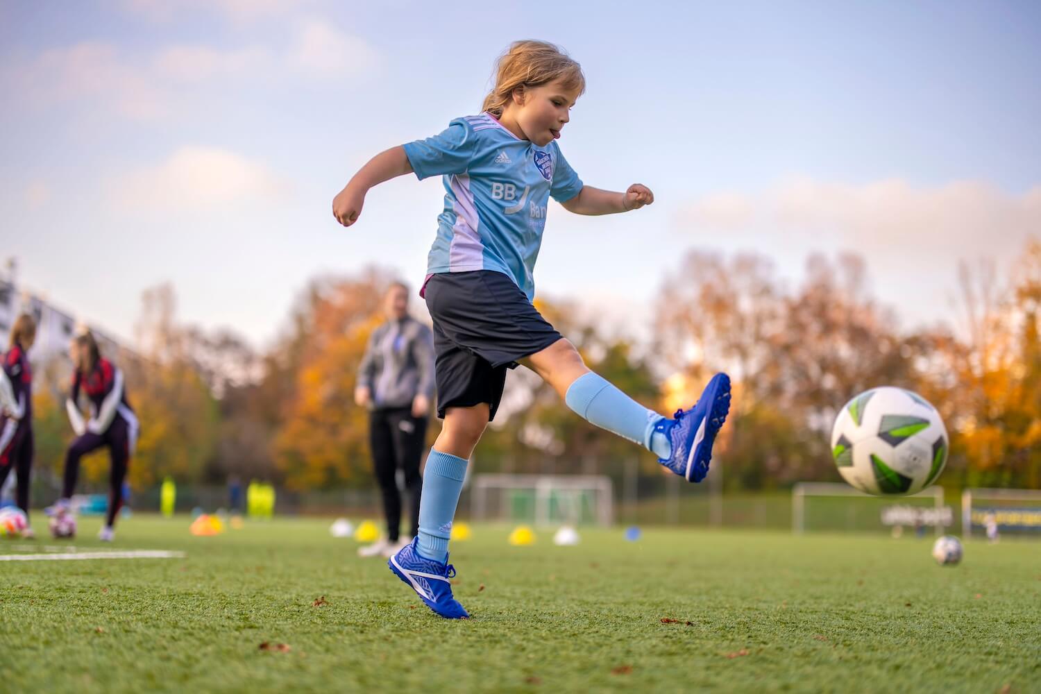 Mädchen in einem hellblauen Trikot schießt gegen einen Ball